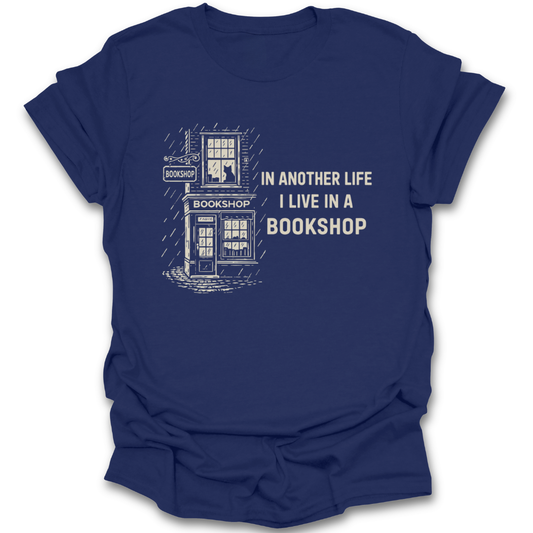 Blue t-shirt with white graphic and text 'In another life I live in a bookshop' on a white background funny book reading literary t shirt