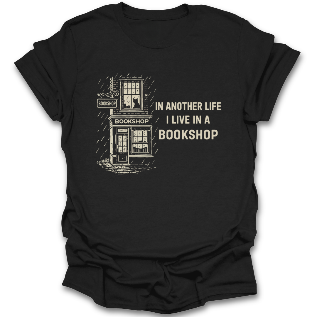 Black t-shirt with a graphic of a bookshop and text 'In another life I live in a bookshop' on a white background. funny book reading literary t shirt