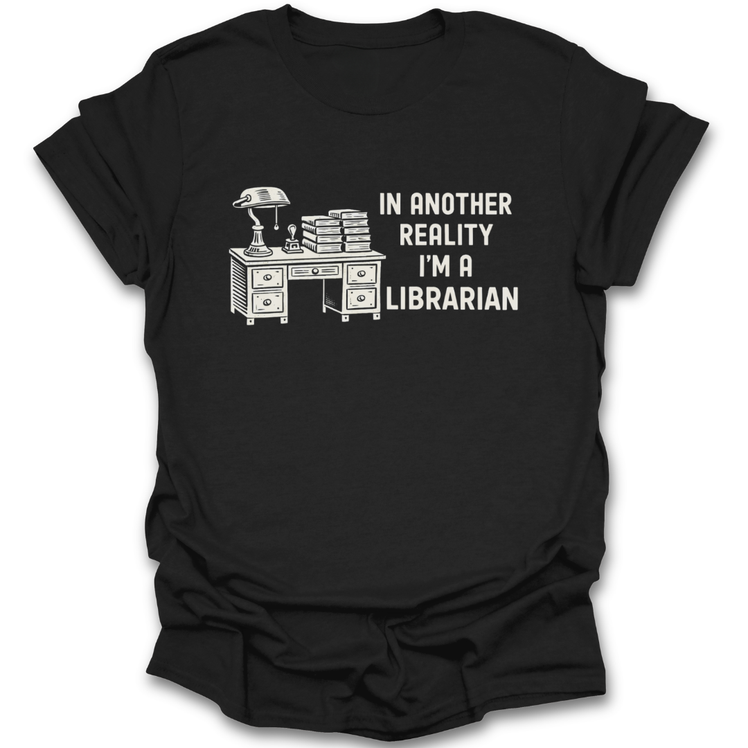 Brown t-shirt with a graphic of a desk and books, and text 'In another reality I'm a librarian' on a white background. funny book reading literary t shirt