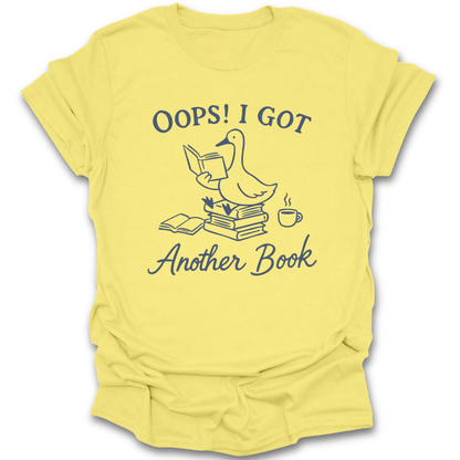 Yellow t-shirt with a graphic of a duck and text 'Oops! I got another book' on a white background. oops i got another book shirt, funny book lover shirt, bookish t-shirt, reader gift, bookworm apparel, bookstore shirt, bibliophile tee, reading humor shirt, book club gift, coffee and books shirt