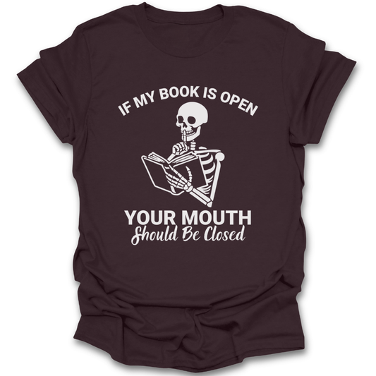 Brown t-shirt with a skeleton reading a book graphic and text on a white background funny book reading literary t shirt