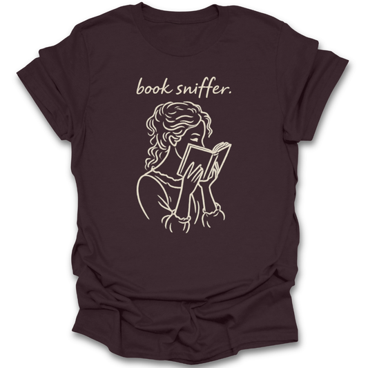 Brown t-shirt with a graphic of a person reading a book and the text 'book sniffer' on a white background. funny book reading literary t shirt