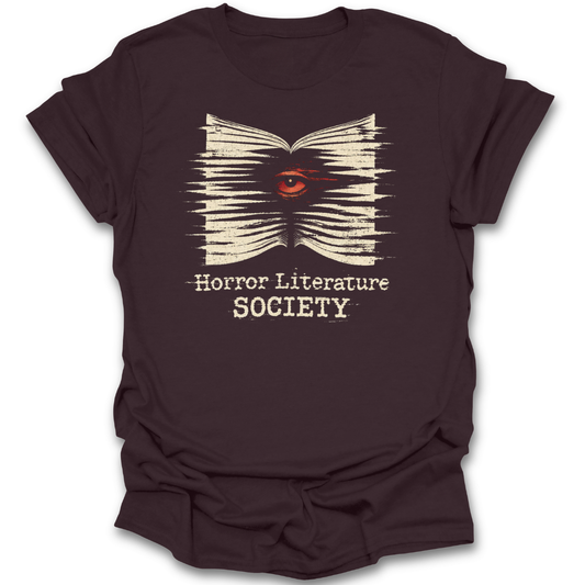 Brown t-shirt with 'Horror Literature Society' design featuring an eye in a book on a white background. horror literature shirt, horror book shirt, book lover shirt, horror reader gift, gothic book shirt, dark academia shirt, spooky bookish shirt, literature society tee, horror books apparel, bookworm shirt.&nbsp;