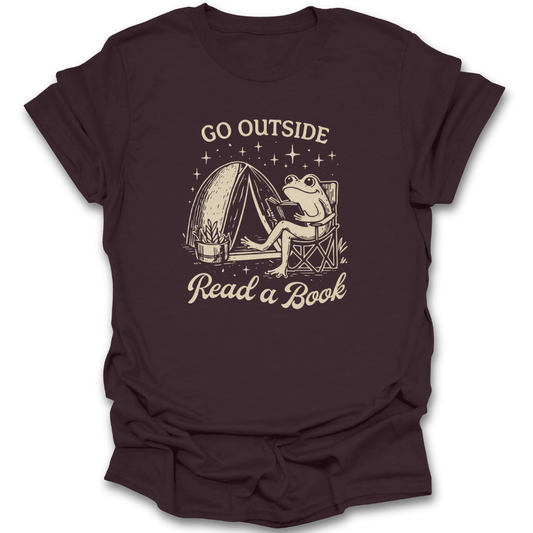 Brown t-shirt with a graphic of a frog reading a book next to a tent and text 'Go Outside Read a Book' on a white background. funny book reading literary t shirt