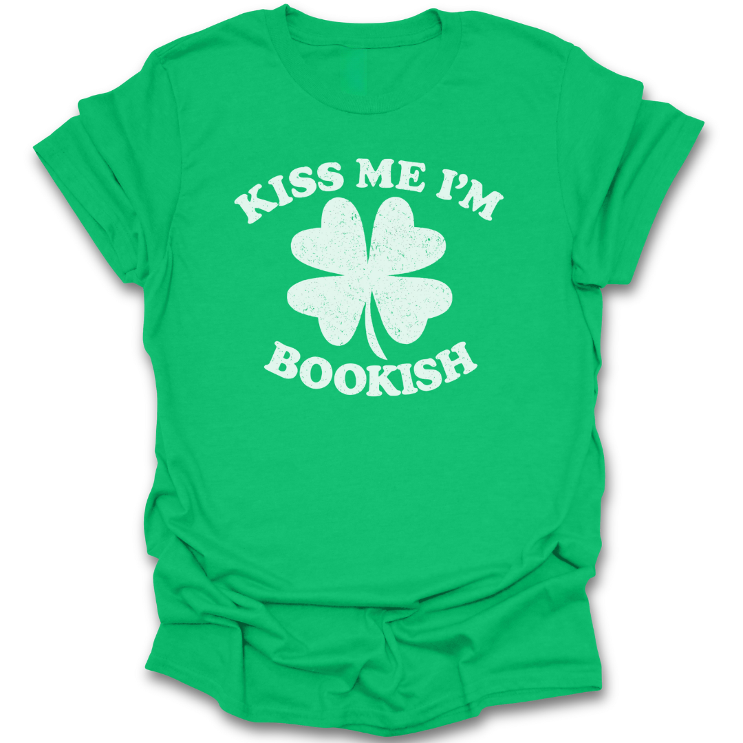 Green t-shirt with white four-leaf clover graphic and text 'Kiss Me I'm Bookish' on a white background st patricks day funny book reading literary t shirt