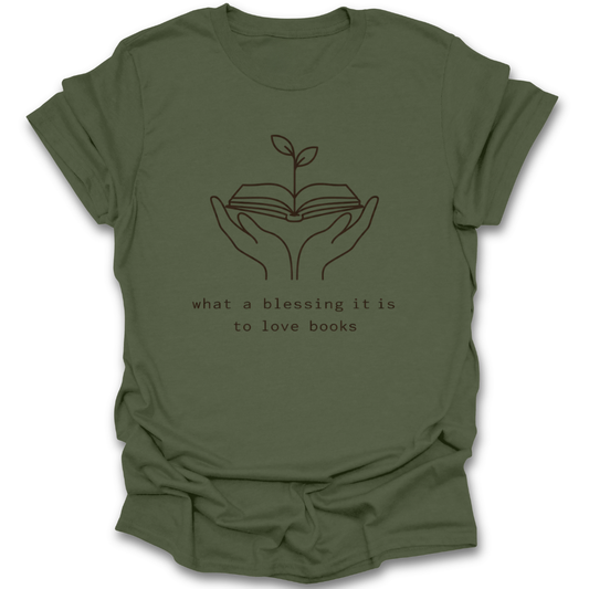 Green t-shirt with a graphic of hands holding an open book with a plant growing out of it and text 'what a blessing it is to love books' on a white background. quote book reading literary t shirt