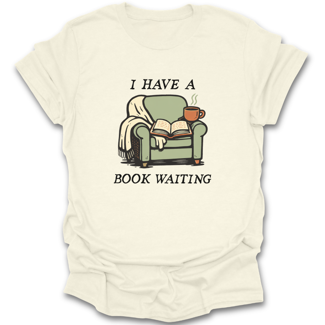 Beige t-shirt with a graphic of a green armchair, book, and cup with text 'I HAVE A BOOK WAITING' on a white background. funny book reading literary t shirt