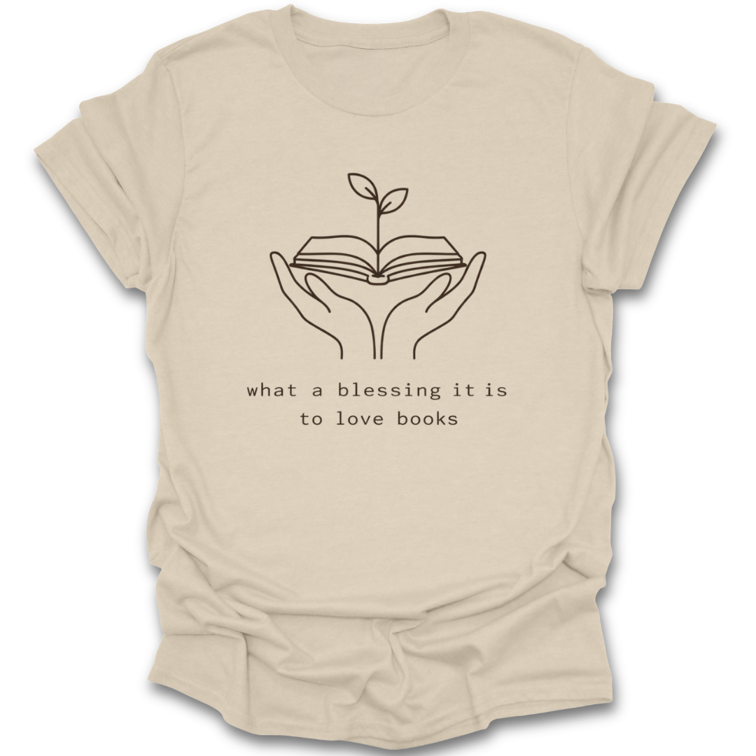 Beige t-shirt with hands holding an open book and a plant, and text 'what a blessing it is to love books' on a white background.  book quote reading literary t shirt
