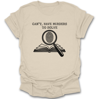 Beige t-shirt with graphic design and text 'Can't, have murders to solve' on a white background true crime murder mystery funny book reading literary t shirt