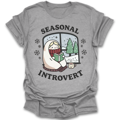 Gray t-shirt with 'Seasonal Introvert' graphic design featuring a person reading a book by a window with trees. funny book reading literary t shirt